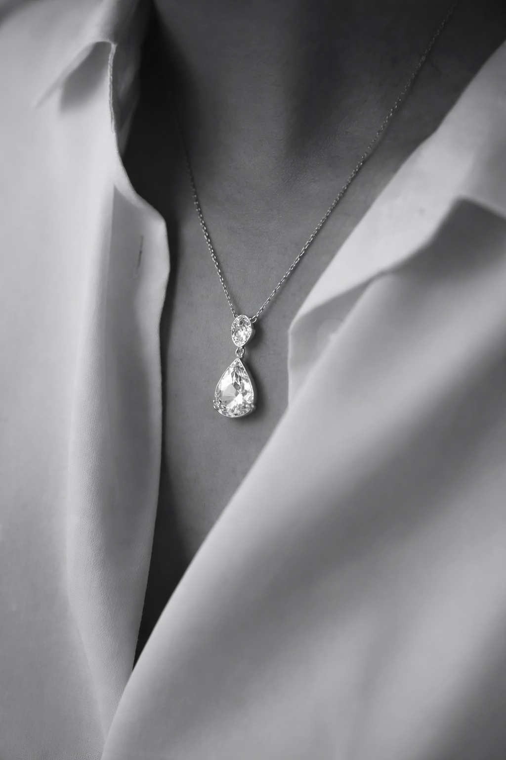 Worn view of a necklace featuring a pear-shaped cubic zirconia drop pendant suspended from a fine chain in a silver tone finish, shown on the neckline.