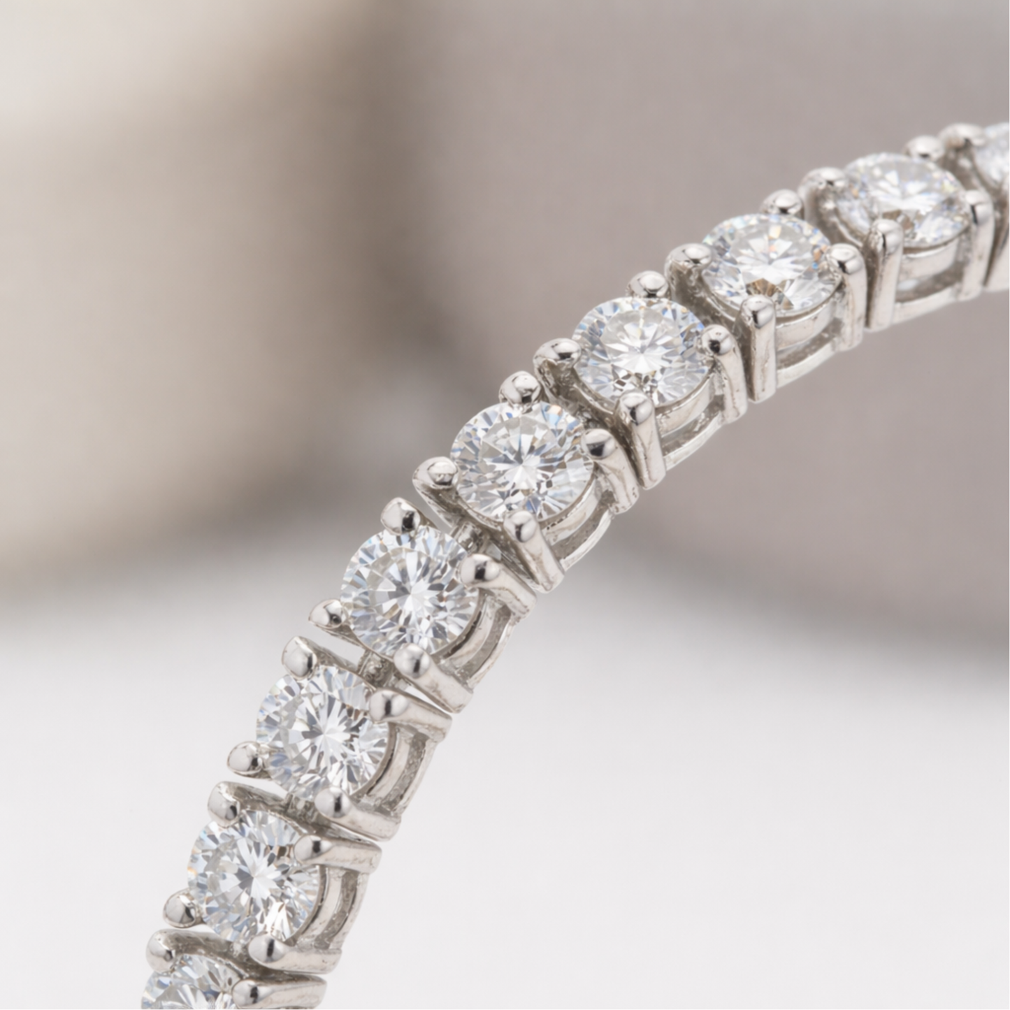 Close up view of round cut cubic zirconia stones set in a continuous silver tone tennis bracelet, highlighting the precise prong setting and brilliant sparkle.
